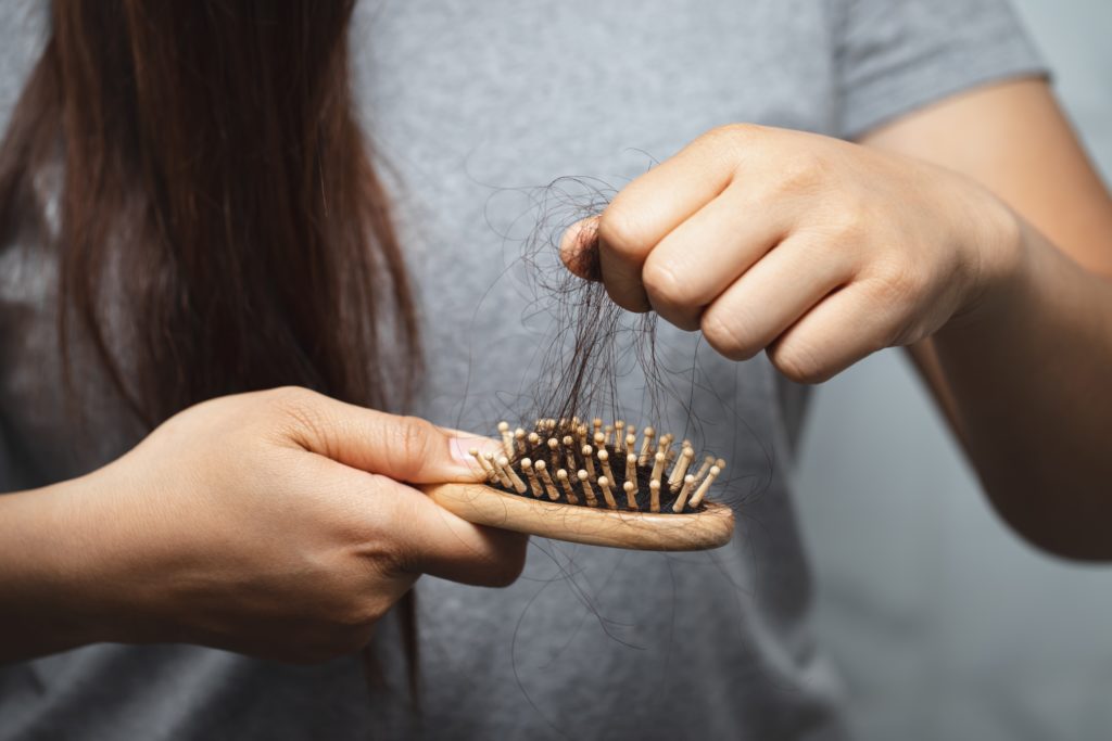 Woman pulls hair out of brush from menopausal hair loss